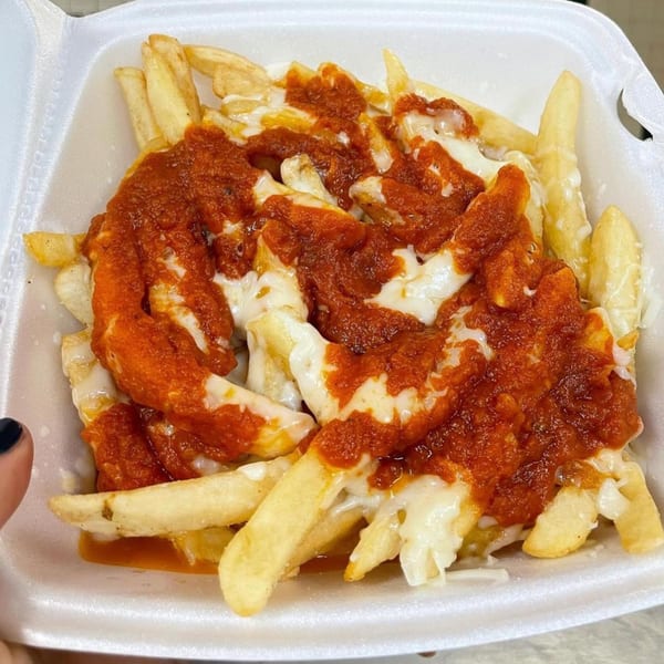 Golden french fries topped with melted cheese and a rich red sauce, served in a white takeout container.